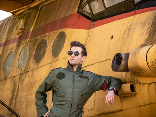 A handsome young pilot standing next to an old plane