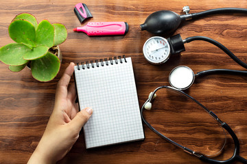 medical concept text writing on white notebook and black stethoscope,  sphygmomanometer on wood table