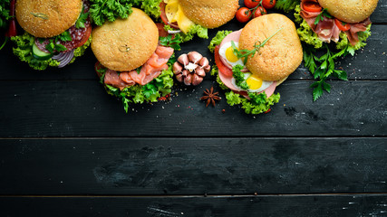 Set of burgers with meat, cheese, fish and vegetables. On a black background. Top view. Free space...