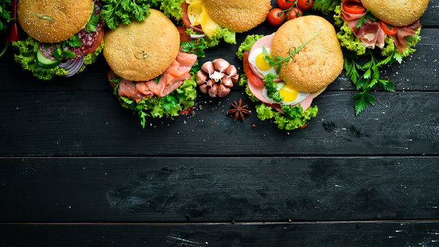 Set of burgers with meat, cheese, fish and vegetables. On a black background. Top view. Free space for your text.