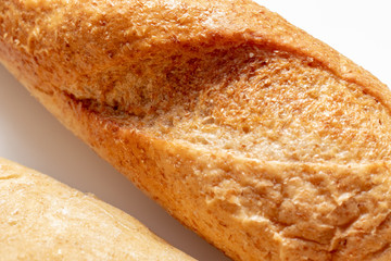 Wheat baked bread with golden crust on white background close up, bakery and grocery concept