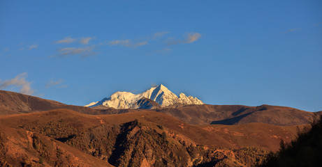 Yala Snow Mountain towering in the distance. Tibet area of Sichuan Province China, Valley covered in golden trees, autumn fall colors. Ganzi Tibetan Plateau Chinese Landscape, Majestic Mountains