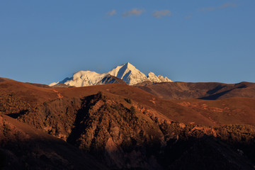 Yala Snow Mountain towering in the distance. Tibet area of Sichuan Province China, Valley covered in golden trees, autumn fall colors. Ganzi Tibetan Plateau Chinese Landscape, Majestic Mountains