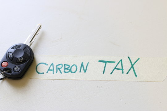 A car key next to a note that says carbon tax. concept of increasing cost to drive or the problems with a carbon tax.