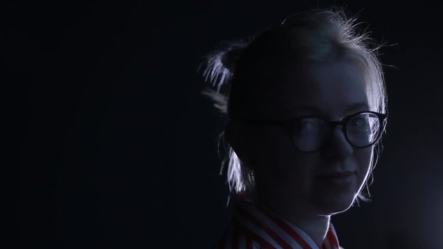 Close-up portrait of young white-haired caucasian girl watching smilingly into camera on black background.