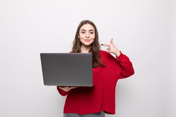Fototapeta premium Smiling young woman holding and pointing on laptop over grey background