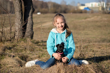 The girl sitting on the ground with a black dog Petit Brabancon early spring