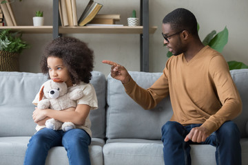 African dad scolding for discipline stubborn daughter sitting on sofa