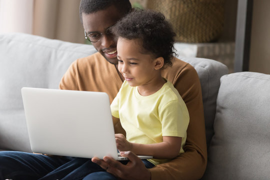 African father and little son sitting on couch with notebook