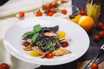 salad with grilled chicken fillet, basil, cherry tomatoes and orange in a white plate.