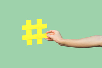 Social media concept, closeup portrait of hand holding large big yellow hash tag sign. Indoor, isolated, copy space, green background, marketing symbol, instagram followers