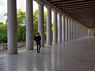 Stoa of Attalos in Athens, Greece. Impressive building in Ancient Agora archeological site. Woman walking away from the camera. Great perspective from columns.