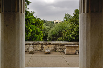 View of trees, temple of Hephaestus and cloudy sky between two columns in Stoa of Attalos in Athens, Greece. Impressive building detail in Ancient Agora archeological site.