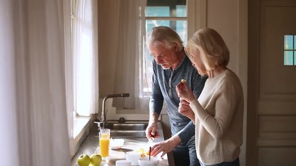 Happy loving senior mature couple having fun preparing healthy breakfast - Powered by Adobe