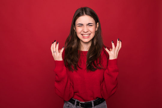 Close up isolated portrait of young annoyed angry woman holding hands in furious gesture on red background. Negative human emotions, face expressions.