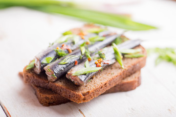 Small fish of sprat with spices on a piece of dark bread