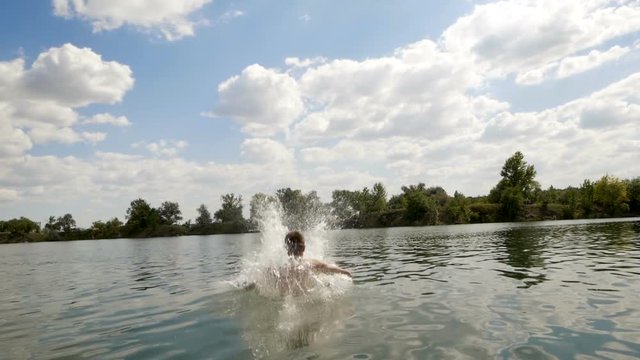 Young man jumping into the lake during calm summer day