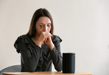 Sad woman with mortuary urn sitting at table