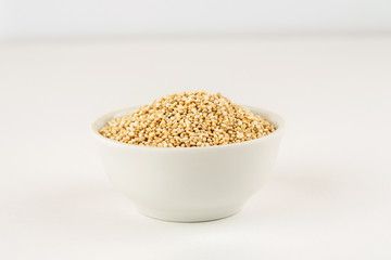 Quinoa raw seeds in white ceramic bowl on a white