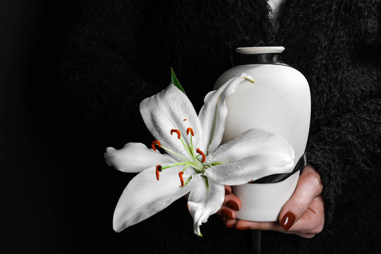 Woman holding mortuary urn with lily flower, closeup