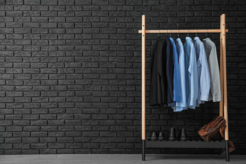 Rack with stylish male clothes near dark brick wall