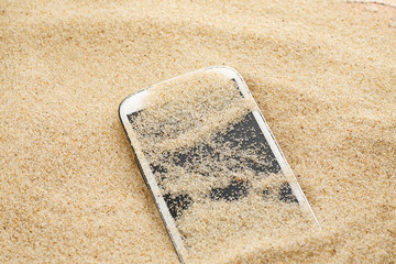 White smartphone lost in sand on the beach