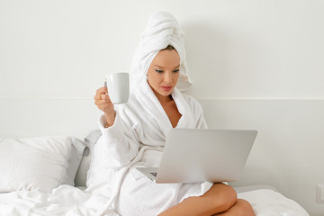 Waking up in a hotel, a young girl, a blogger, gladly does her job with a cup of freshly brewed coffee.