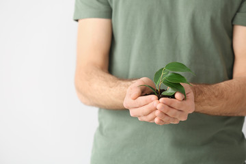 Man with young plant on light background, closeup