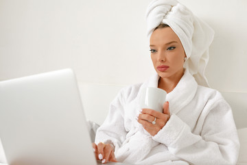 Waking up in a hotel, a young girl, a blogger, gladly does her job with a cup of freshly brewed coffee.