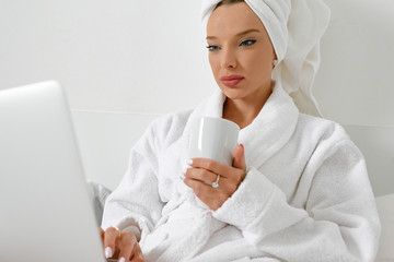 Waking up in a hotel, a young girl, a blogger, gladly does her job with a cup of freshly brewed coffee.