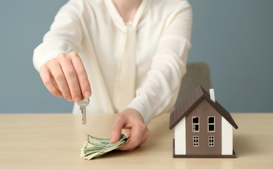 Real estate agent with key, money and model of house at table