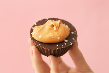 Female hand with chocolate butter cup on color background