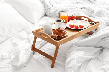 Table with tasty breakfast on bed
