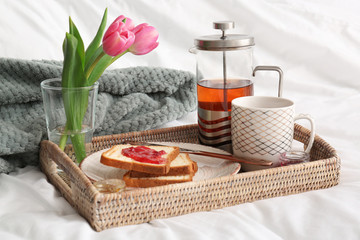 Obraz na płótnie Canvas Tray with tasty breakfast and flowers on bed