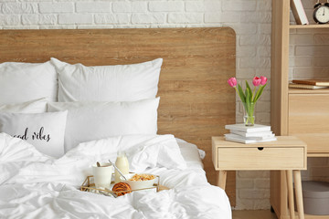 Tray with tasty breakfast on bed in interior of room