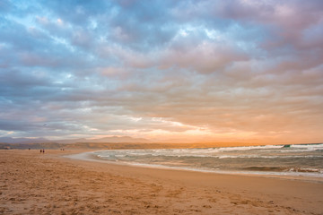 Fototapeta na wymiar Rays of golden evening light falling on the Plettenberg Bay beach at sunset, with mountains in the distance. Garden Route, Western Cape, South Africa