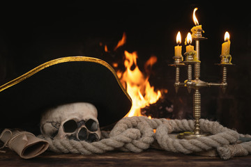 Pirate table with human skull, moorings, captain hat, book and scroll map on a burning fire...