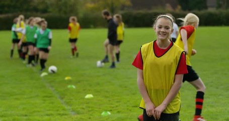 4K Portrait smiling girl at soccer training, with team mates training in background. Slow motion.