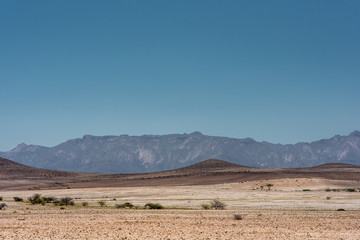 Brandberg mountain under a blue sky, with arid and sandy foreground. Namibia