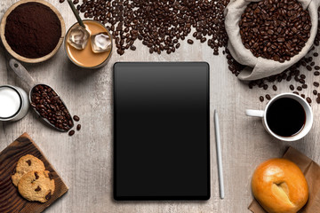 Above view of computer tablet with coffee shop ingredients in cafe, blank screen copy space
