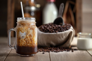 Cold brew iced coffee with milk cream swirls on a rustic wood table with coffee beans, copy space