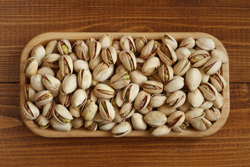 Salted dried pistachio nuts in bamboo plate on wooden background. View from above