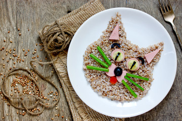 Fun food for children - healthy buckwheat porridge shaped cat face on white plate top view
