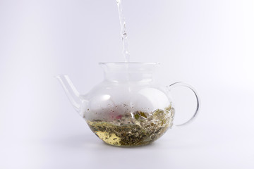 Pouring hot water to the glass teapot with herbal tea, isolated on white background
