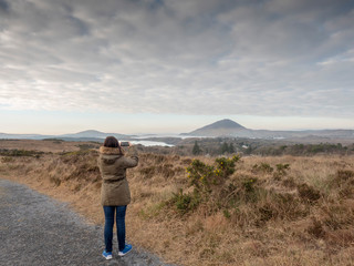 Woman taking picture on her smart phone in Connemara national park, county Galway, Ireland.