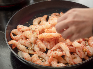 Frying pan with prawns, cook adds spices and herbs.