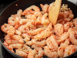 Prawns on a frying pan, Cook stirring dish with wooden stick.