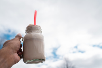 hand holding milkshake in mason jar in front of sky - 264850910