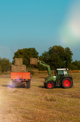 green tractor loading hay bales on a trailer