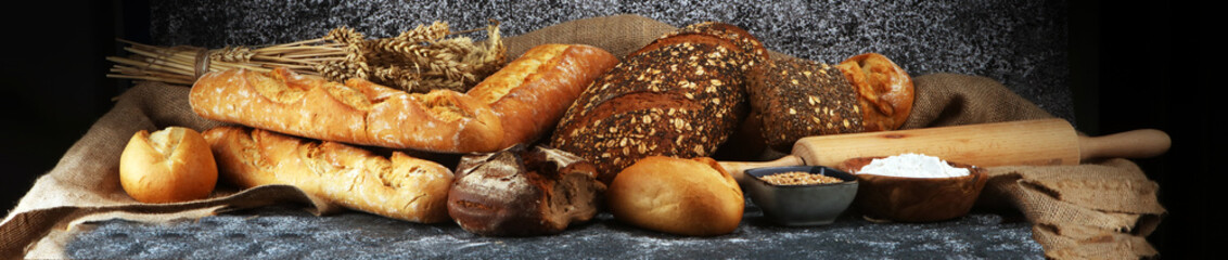 Assortment of baked bread and bread rolls on rustic grey bakery table background